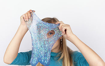 Funny girl holding a glitter slime in front of her face and looking through its hole.